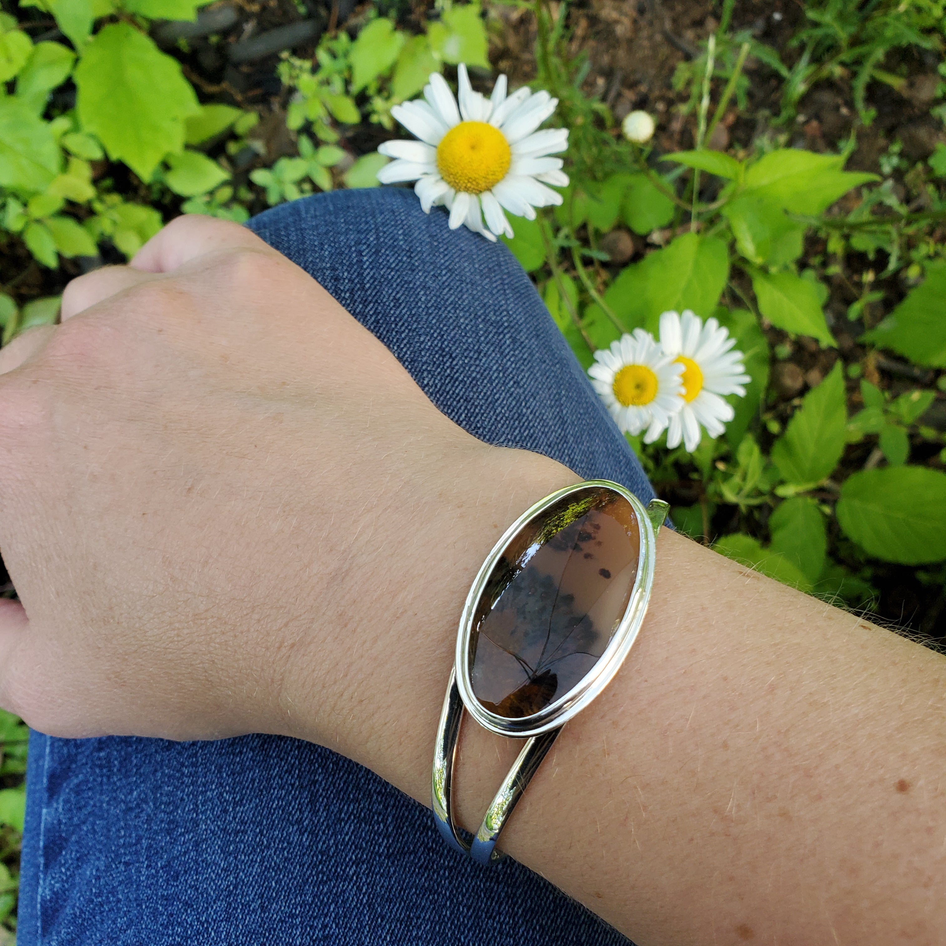 Long oval agate sterling silver cuff bracelet shown on wrist with daisies in background