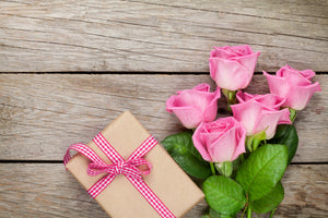Photo of a wrapped box with 5 pink roses next to it